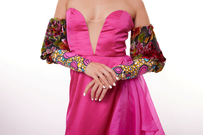 Robe bustier fluide rose et fuchsia avec un décolleté plongeant, manches amovibles ornées d’un motif floral et wax coloré, et jupe asymétrique.